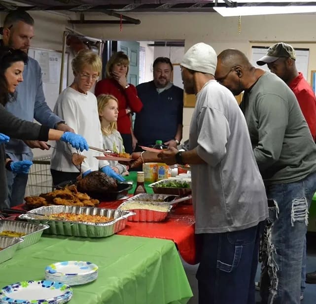 A group of people standing around a table with food.