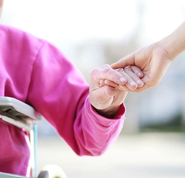 A person holding another persons hand while sitting on a stroller.